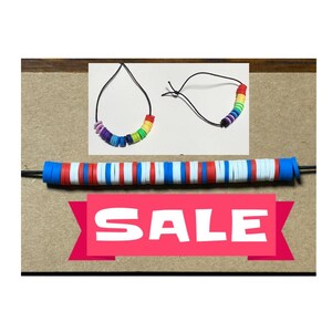 May include: A collection of colorful beaded necklaces and a beaded strand. The necklaces feature rainbow-colored beads and a black cord. The strand has blue, red, and white beads. A pink banner with the word "SALE" is also visible.