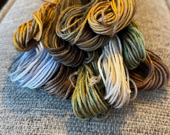 May include: A bundle of embroidery floss in shades of brown, green, beige, and blue. The floss is wound around cardboard spools.