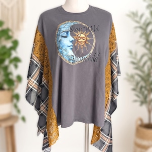 May include: A charcoal grey t-shirt featuring a graphic of a blue crescent moon and a golden sun with the text Stay Wild Moonchild. The sides are accented with panels of mustard yellow lace and a grey, white, and black plaid fabric pattern.