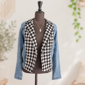 Peut inclure: Une veste composée de manches et de panneaux arrière en jean bleu, associés à un panneau avant à motif pied-de-poule noir et blanc. Le vêtement présente un col à revers cranté et des manches longues, présenté sur un buste de mannequin marron.