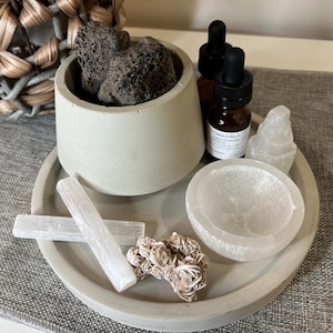 May include: A gray concrete tray with a smaller gray concrete bowl, a white selenite bowl, two selenite sticks, a selenite tower, and a rose quartz cluster. Two small glass bottles with dropper tops are also on the tray. The bottles have labels that read "Citrus & Mint" and "Lemon Eucalyptus".