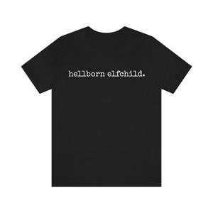 May include: Black t-shirt with the white text "hellborn elfchild." The short-sleeved shirt is made of a soft material and has a crew neck. The text is centered on the chest.