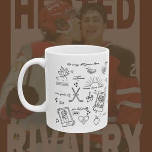 May include: White ceramic mug with black line art illustrations, including a maple leaf, duck, crossed hockey sticks, and a polaroid photo. The mug has the text "It's scary but you're here" and other phrases. The background features two hockey players.