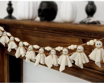 May include: A Halloween-themed garland featuring small, white ghost figures with simple facial details and twine accents. The ghosts are strung together with wooden beads, creating a festive and decorative piece.