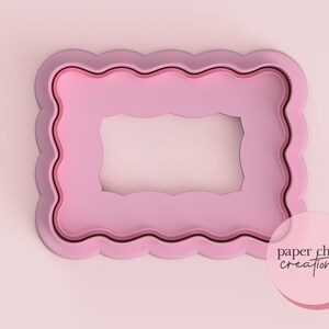 May include: Pink plastic cookie cutter in the shape of a scalloped rectangle with a smaller scalloped rectangle cut out in the centre. The cookie cutter is on a pink background. The text "paper chain creations" is visible in the bottom right corner of the image.