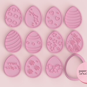 May include: Twelve pink plastic Easter egg cookie cutters with various designs, including polka dots, stars, hearts, flowers, stripes, and a bow. The cutters are arranged in three rows of four on a pink background. The text "paper chain creations" is visible in the bottom right corner.