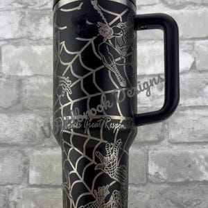 Puede incluir: Vaso negro con un dise&ntilde;o plateado de Spider-Man, que incluye un patr&oacute;n de telara&ntilde;a y el superh&eacute;roe. El vaso tiene un asa y tapa negras, y el texto "With Great Responsibility" es visible.