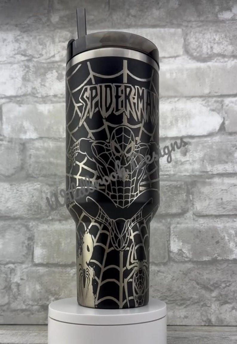 Puede incluir: Vaso aislado negro y plateado con un dise&ntilde;o de Spider-Man. El vaso tiene un cuerpo negro con un gr&aacute;fico plateado de Spider-Man, telara&ntilde;as y la palabra "SPIDER-MAN". Incluye una tapa y una pajita negras.