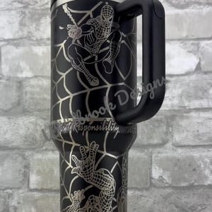 Puede incluir: Vaso t&eacute;rmico negro con asa, con un dise&ntilde;o de Spider-Man grabado en plata. El dise&ntilde;o incluye a Spider-Man en acci&oacute;n con su telara&ntilde;a y el texto "With Great Responsibility". El vaso tiene tapa y pajita negras.