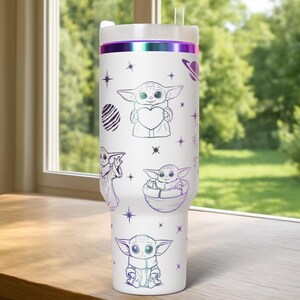 Puede incluir: Vaso blanco con tapa y pajita, con ilustraciones de un personaje sosteniendo un coraz&oacute;n, en una c&aacute;psula y otras poses. El dise&ntilde;o incluye estrellas y un planeta. El borde superior tiene una banda iridiscente p&uacute;rpura y verde.