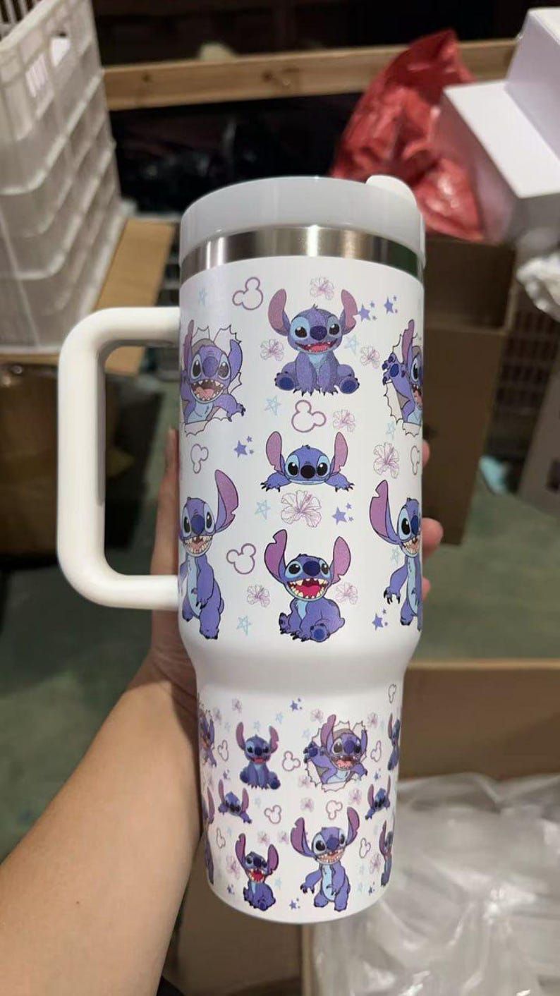 Op de afbeelding: Witte ge&iuml;soleerde beker met een herhaald patroon van het personage Stitch uit Lilo & Stitch. De beker heeft een witte handgreep en deksel. Het ontwerp bevat Stitch, bloemen en sterren. Geschikt voor warme en koude dranken.
