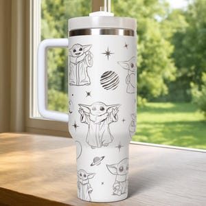 Puede incluir: Vaso t&eacute;rmico blanco con asa, con un patr&oacute;n repetido de un personaje de dibujos animados en varias poses, junto con estrellas y planetas. El vaso tiene una tapa y un asa blancas, y una banda plateada cerca de la parte superior.