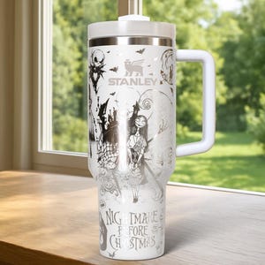 Puede incluir: Vaso Stanley blanco con un dise&ntilde;o de "Pesadilla antes de Navidad". El vaso tiene un asa y tapa blancos, y un gr&aacute;fico plateado de Jack Skellington, Sally y otros personajes. El texto "NIGHTMARE BEFORE CHRISTMAS" est&aacute; impreso en la parte inferior.
