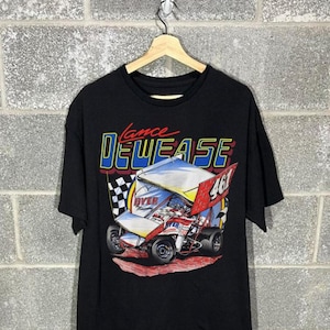 May include: A black short-sleeve t-shirt featuring a graphic print of a sprint car with the number 461 on the side. The text "Lance" is printed in red above the blue and yellow "DEWEASE" lettering. A checkered flag is visible behind the race car.