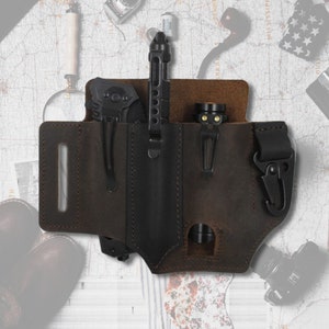 May include: A brown leather carrying case with three pockets for holding a pen, a knife, and a torch. The case has a belt loop and a snap hook.