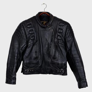 May include: Black leather motorcycle jacket with quilted shoulder and upper arm detailing. It has a diagonal zip, multiple zipped pockets, and adjustable waist straps with buckles. The collar is a stand-up style with a snap closure.