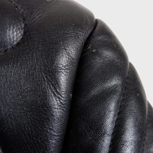 May include: Close-up of black leather with a quilted pattern. The leather has a textured surface and visible stitching. The image highlights the details of the material, showcasing its quality and craftsmanship.
