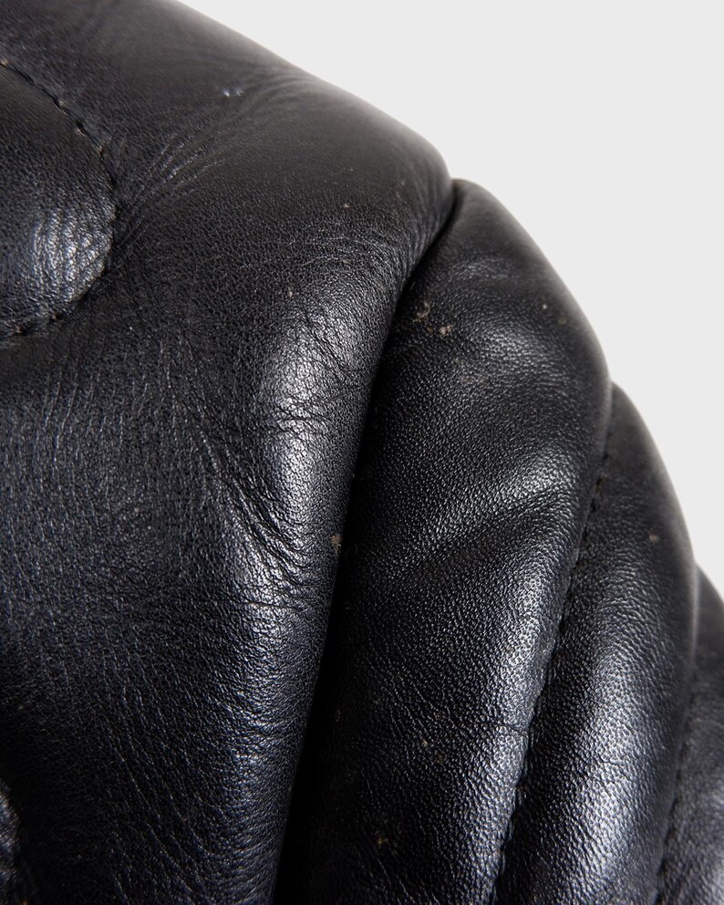 May include: Close-up of black leather with a quilted pattern. The leather has a textured surface and visible stitching. The image highlights the details of the material, showcasing its quality and craftsmanship.