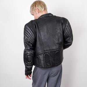 May include: Black leather motorcycle jacket with quilted shoulder and elbow padding. The jacket has a classic design with a stand-up collar and a fitted silhouette. The back of the jacket features a unique padded design.