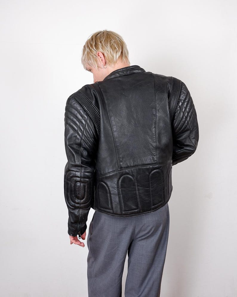 May include: Black leather motorcycle jacket with quilted shoulder and elbow padding. The jacket has a classic design with a stand-up collar and a fitted silhouette. The back of the jacket features a unique padded design.