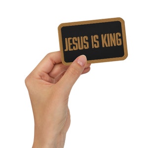 May include: A brown patch with a black background and the text "JESUS IS KING" in gold embroidery.