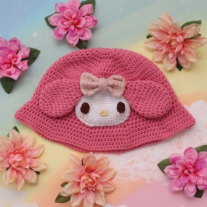 May include: Pink crocheted sun hat with a white crocheted Hello Kitty character design.