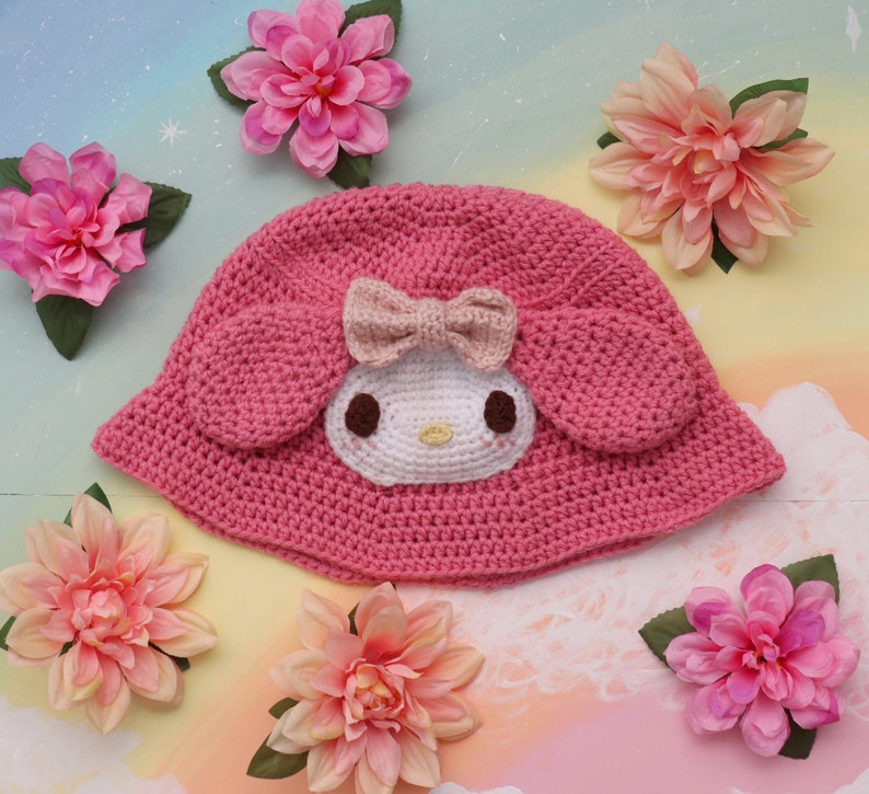 May include: Pink crocheted sun hat with a white crocheted Hello Kitty character design.