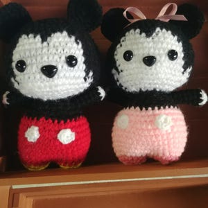 May include: Two crocheted dolls, resembling cartoon characters. The male doll has red shorts with white polka dots. The female doll has pink shorts and a pink bow. Both dolls have black and white features. The dolls are handmade.