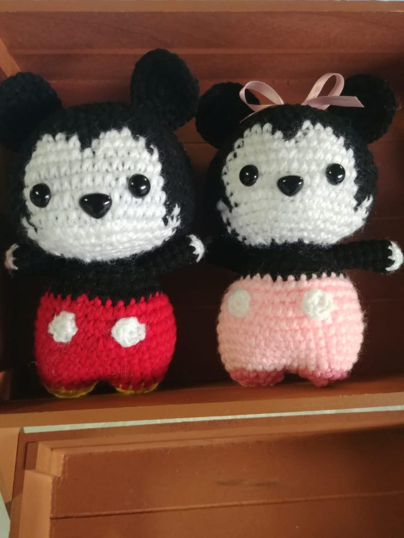 May include: Two crocheted dolls, resembling cartoon characters. The male doll has red shorts with white polka dots. The female doll has pink shorts and a pink bow. Both dolls have black and white features. The dolls are handmade.