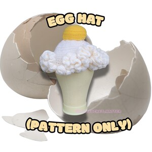 Könnte beinhalten: Ein gehäkelter Eierhut mit gelbem Eigelb und weißem Eiweiß-Design, dargestellt in einer zerbrochenen Eierschale. Der Text "EGG HAT" und "(PATTERN ONLY)" sind sichtbar.
