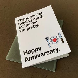 Puede incluir: Una tarjeta blanca con texto negro que dice "Gracias por alimentarme y decirme que soy bonita. Feliz aniversario." Una ilustraci&oacute;n simple de un plato, un tenedor y un cuchillo con un coraz&oacute;n rojo en el plato est&aacute; debajo del texto.