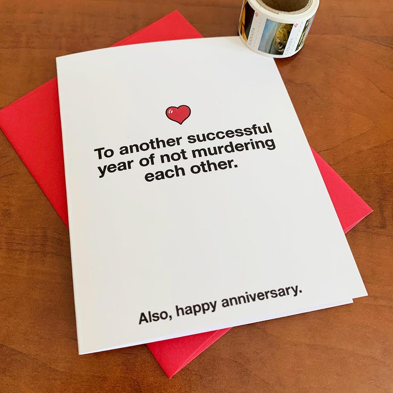 Puede incluir: Una tarjeta blanca con un coraz&oacute;n rojo y el texto "Para otro a&ntilde;o exitoso sin asesinatos mutuos. Tambi&eacute;n, feliz aniversario."