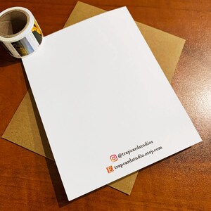 May include: A white card with the text "@trapcardstudios" and "trapcardstudio.etsy.com" printed on it. The card is on a brown surface.
