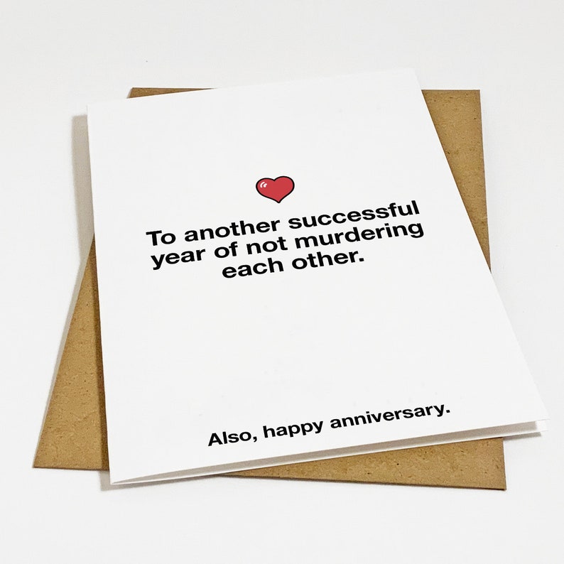 Puede incluir: Una tarjeta blanca con un coraz&oacute;n rojo y el texto "Para otro a&ntilde;o exitoso sin asesinatos mutuos. Tambi&eacute;n, feliz aniversario."