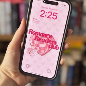 May include: A pink and white phone screen with a pink heart pattern. The screen displays the text "Romance Readers Club" with a pink and white hot air balloon graphic. The time is 2:25 and the date is Sunday, 9 February.