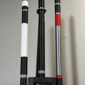 May include: Three vertical poles with varying color schemes. One is black and white, another is solid black, and the third is silver with red and black accents. Each pole has a unique design and texture, suggesting a modern aesthetic.