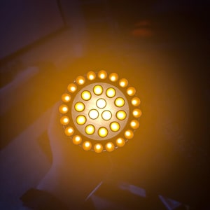 May include: A circular light fixture with numerous small, evenly spaced, yellow-orange lights. The lights are arranged in a circular pattern, with a brighter central cluster. The fixture emits a warm glow, suggesting a decorative or functional lighting element.
