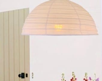 May include: A white dome-shaped paper pendant light fixture hangs from a thin cord. The shade features horizontal ribbed detailing and a visible warm light bulb glowing from within the center of the translucent paper structure.