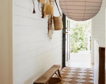 May include: A hallway scene featuring a rustic wooden bench with a woven basket, a diamond-patterned rug, and a row of straw hats hanging on the wall. A large, round paper lantern hangs from the ceiling, illuminating the space.