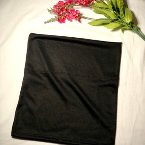 May include: A black fabric tube, possibly a headband or hair scarf, folded and lying flat on a white surface.