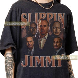 Peut inclure: T-shirt gris foncé avec un graphisme de style vintage représentant un homme en costume, avec les mots "SLIPPIN JIMMY" en marron. Le design comprend plusieurs images de la même personne.