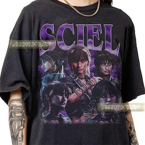 May include: Dark gray t-shirt featuring a graphic design with the word "SCIEL" in purple, with multiple images of a person. The design has a vintage, distressed look.
