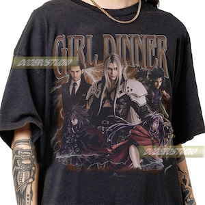 May include: Dark gray t-shirt featuring a graphic of anime characters with the text "GIRL DINNER" in a distressed font. The image includes multiple characters with long hair and detailed clothing, set against a backdrop of lightning.