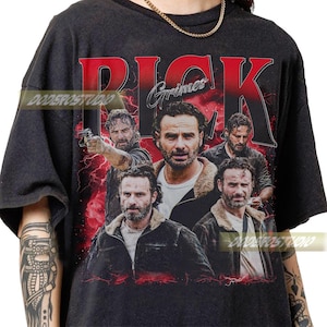 May include: Black t-shirt featuring a collage of images of a man with a beard, with the name "Rick Grimes" in red block letters. The design includes a red lightning bolt background.