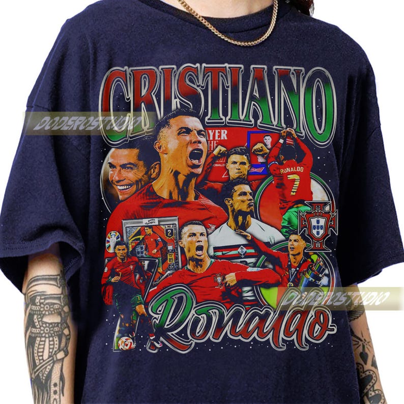 May include: Navy blue t-shirt featuring a collage of images of Cristiano Ronaldo, with the name "Cristiano" in green and red lettering. The word "Ronaldo" is in a cursive font. The shirt has a vintage, distressed look.