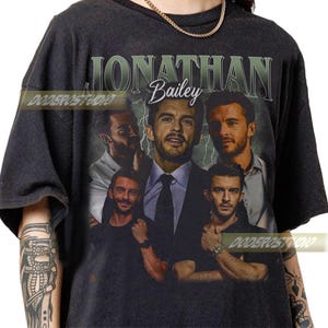 May include: Dark gray t-shirt featuring a collage of images of Jonathan Bailey. The design includes the name "Jonathan Bailey" in a vintage font, with the word "Bailey" in cursive. The shirt has a vintage, distressed look.