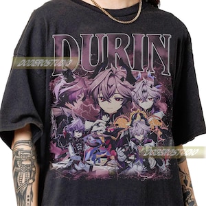 May include: Dark gray t-shirt featuring the word "DURIN" in a purple, stylized font above a graphic of anime characters in shades of purple, white, and black. The design has a vintage, distressed look.
