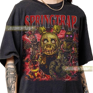 May include: Dark gray t-shirt featuring a graphic of Springtrap and other characters from the Five Nights at Freddy's franchise. The word "SPRINGTRAP" is printed in red across the top. The design includes a detailed illustration with a horror theme.
