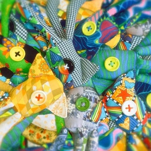 May include: A close-up of a collection of colorful fabric dolls. Each doll features a unique patchwork design with various patterns, including floral, geometric, and houndstooth. Large, decorative buttons in yellow, green, and black secure the pieces.