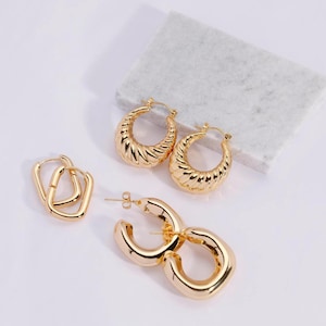 May include: Set of four gold hoop earrings. Two pairs of large hoops with a textured design and two pairs of smaller square hoops.